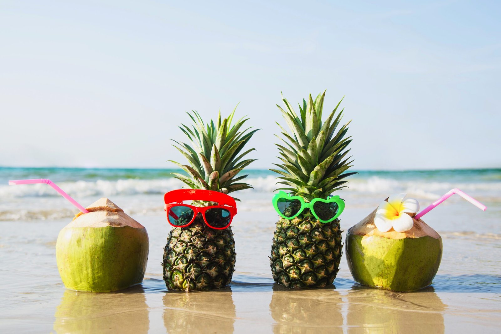 Fresh coconut and pineapple put sun lovely glasses on clean sand beach with sea wave background - fresh fruit with sea sand sun vacation background concept